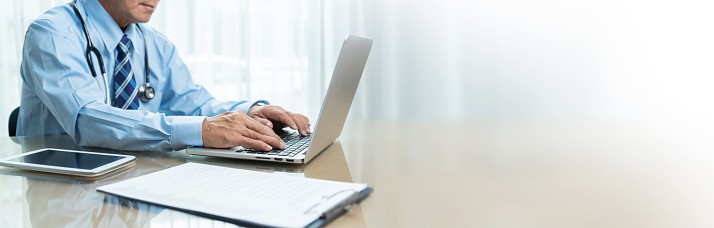 Close up of physician sitting at a desk and typing on a laptop