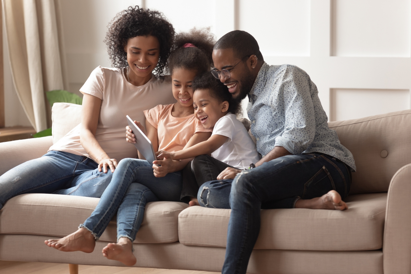 A family sits on a couch and gathers around a tablet