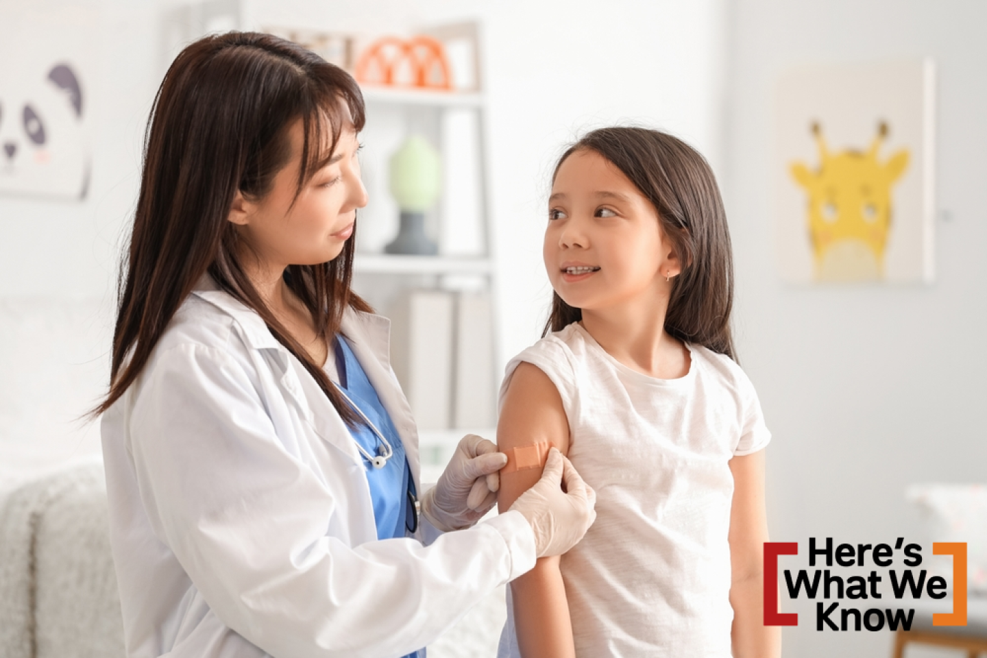 Female Asian doctor applying medical patch on little girl's arm after vaccination in clinic