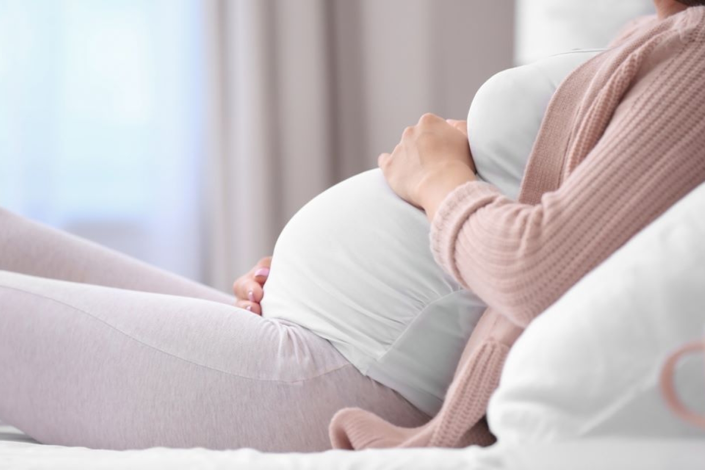 Young pregnant woman lying on bed and touching her belly at home, closeup