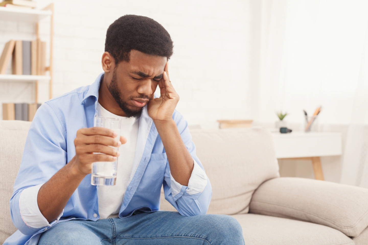Exhausting headache. Sick african-american man taking pill with glass of water, suffering from migraine at home, copy space
