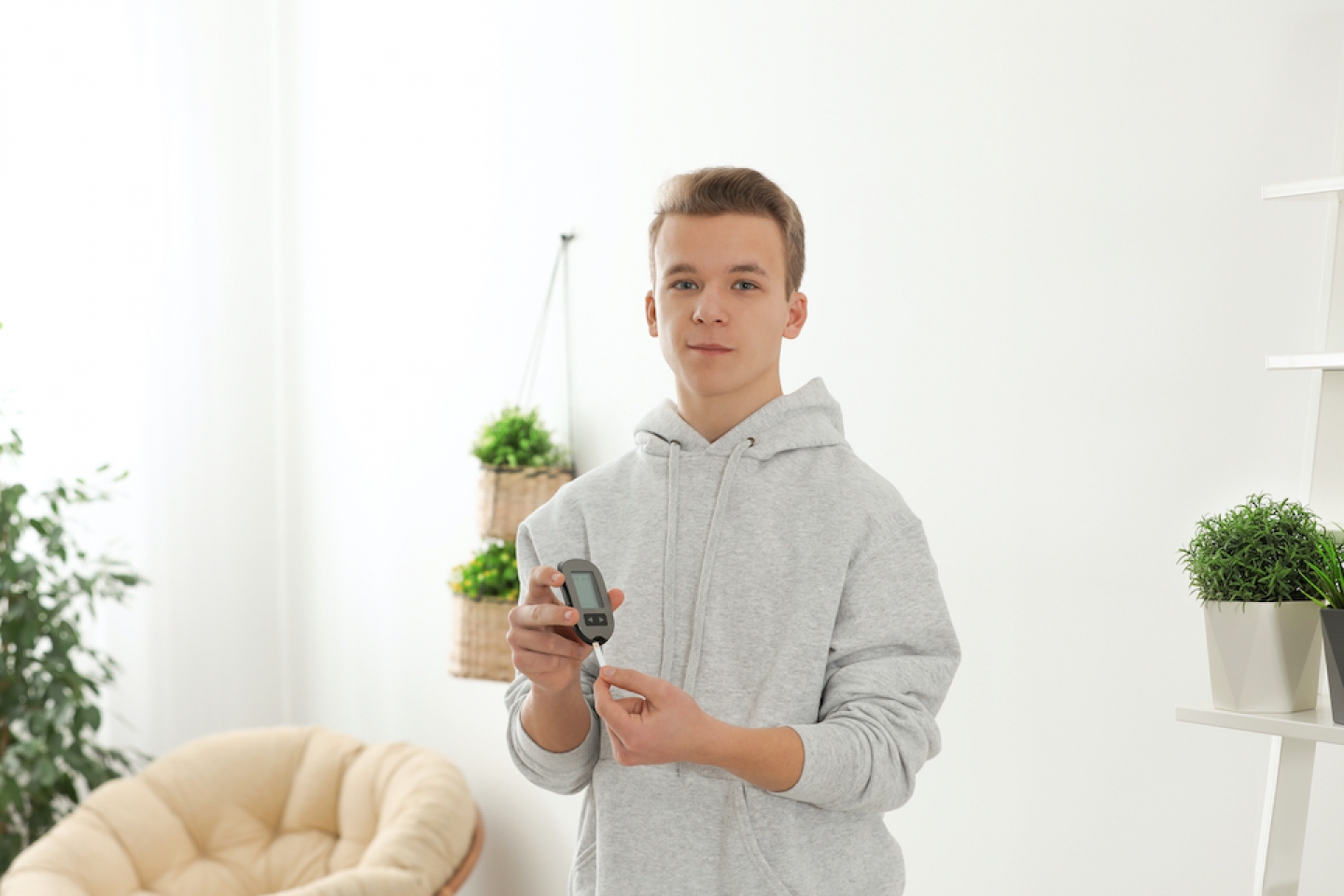 Teen boy holding digital glucometer at home