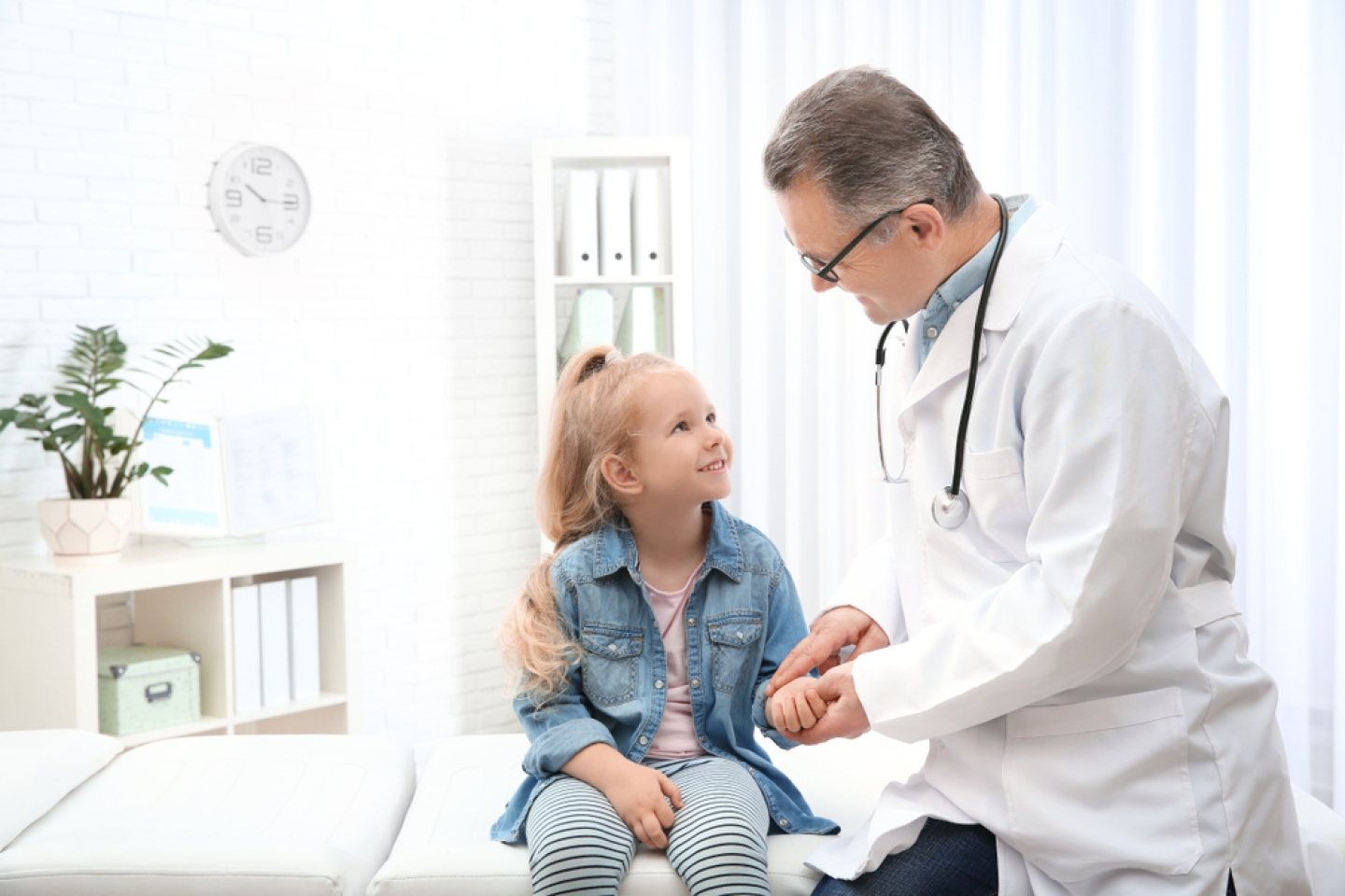 Doctor checking little girl's pulse with fingers in hospital.