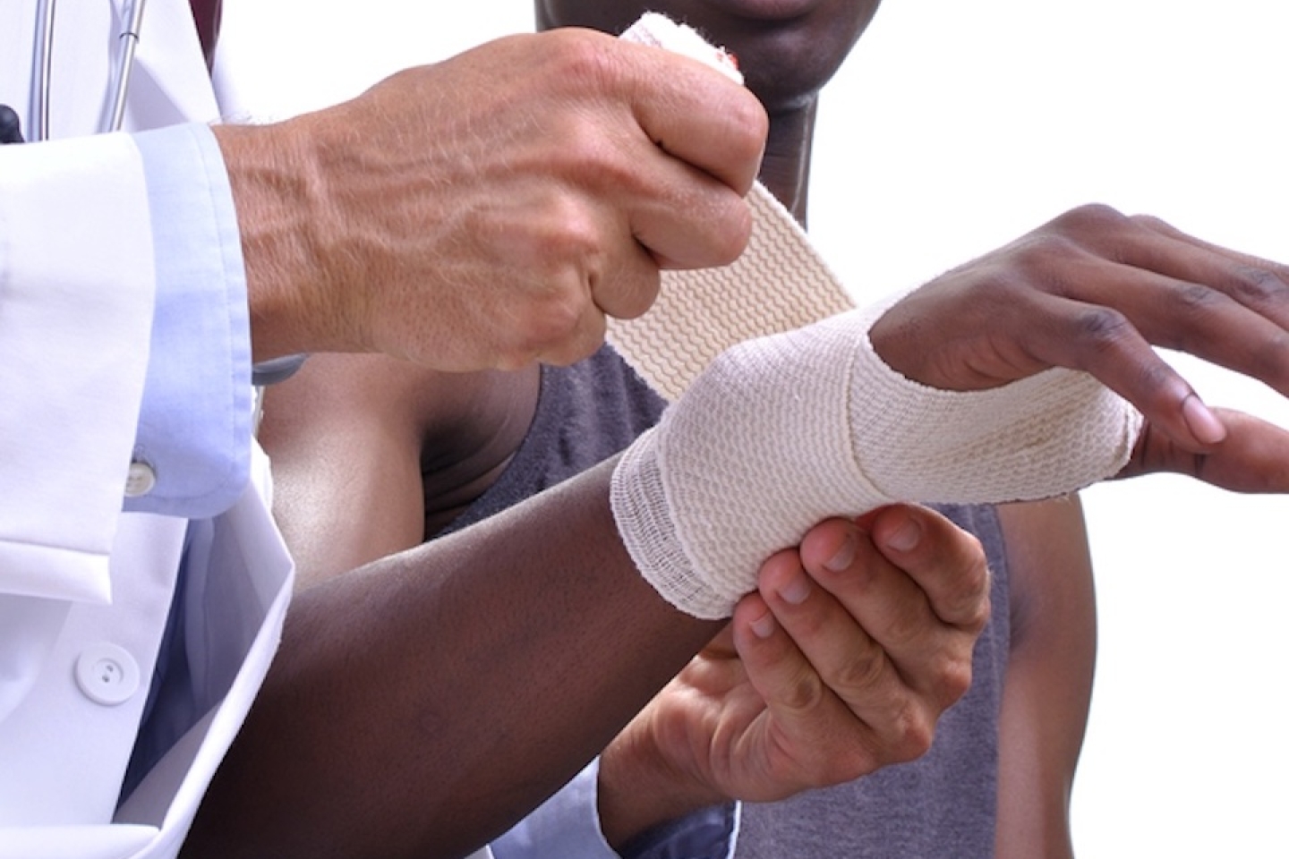 Male medical doctor wraps injured wrist of male patient with a sports bandage on white background