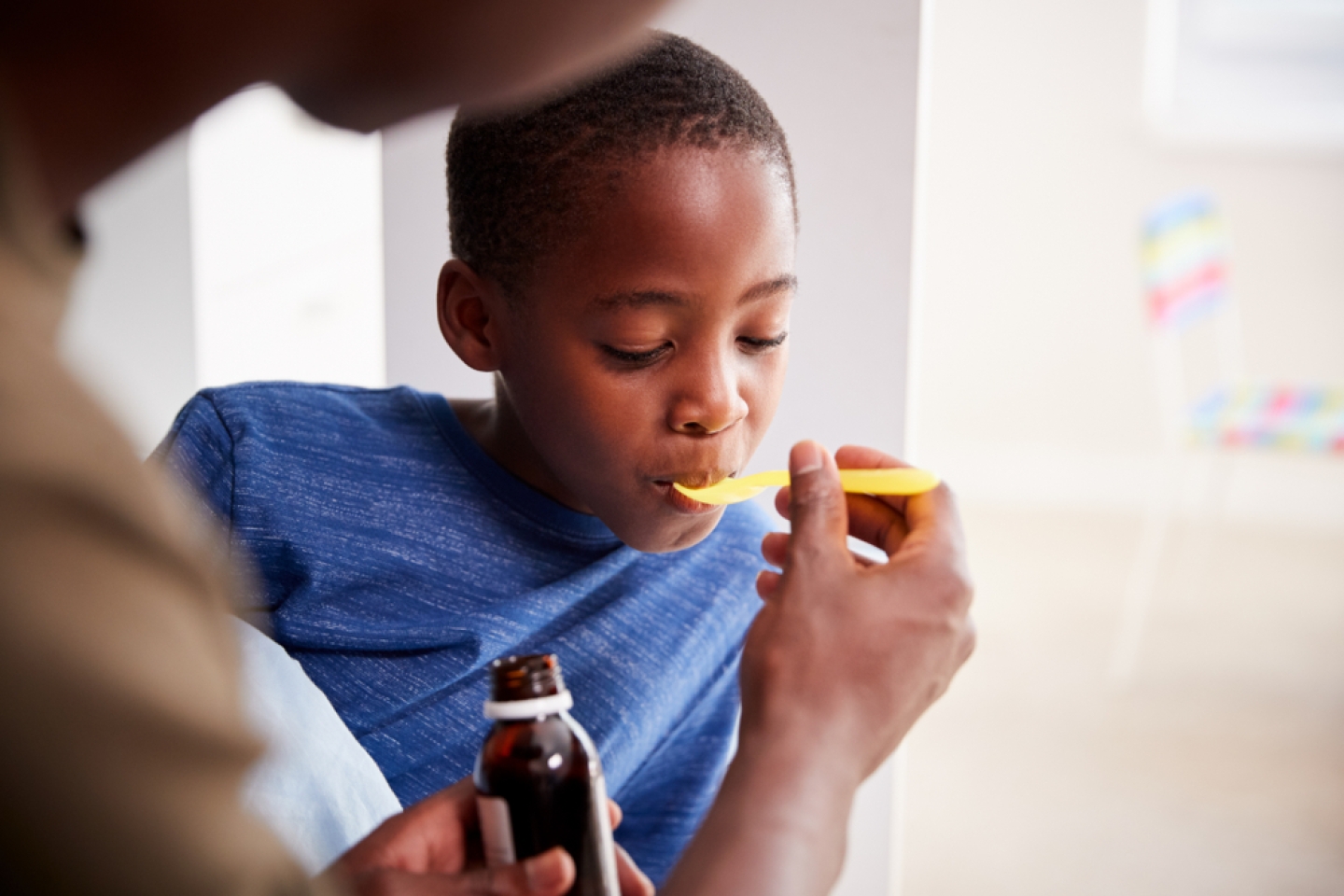 Father Giving Sick Son Ill In Bed Medicine From Bottle