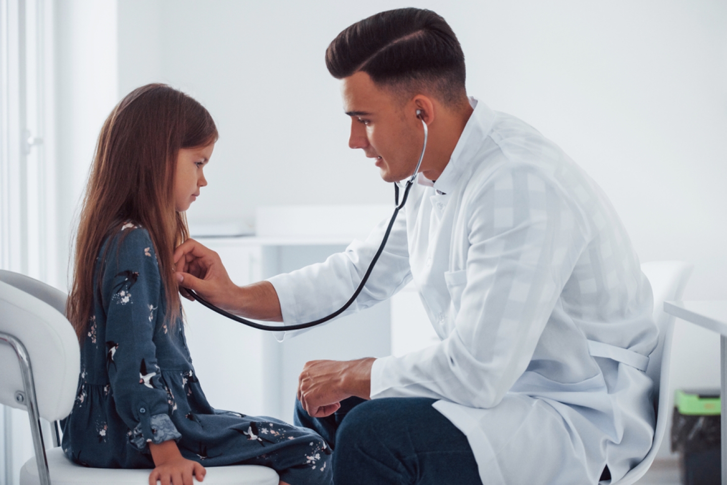 Young pediatrician works with little female visitor in the clinic.