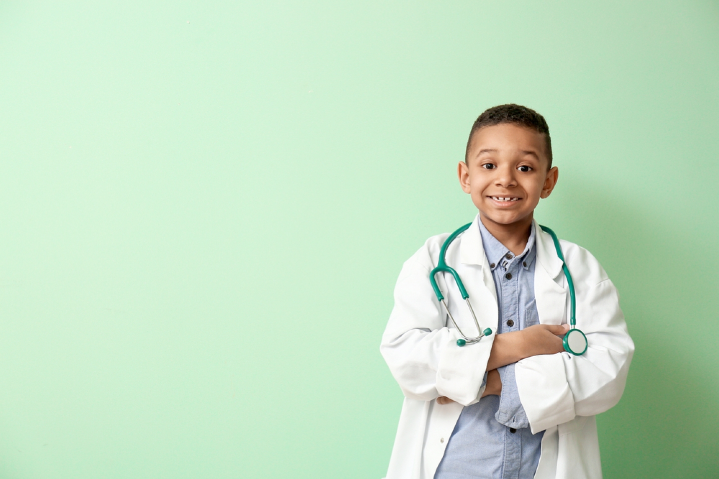 Cute little African-American doctor on color background