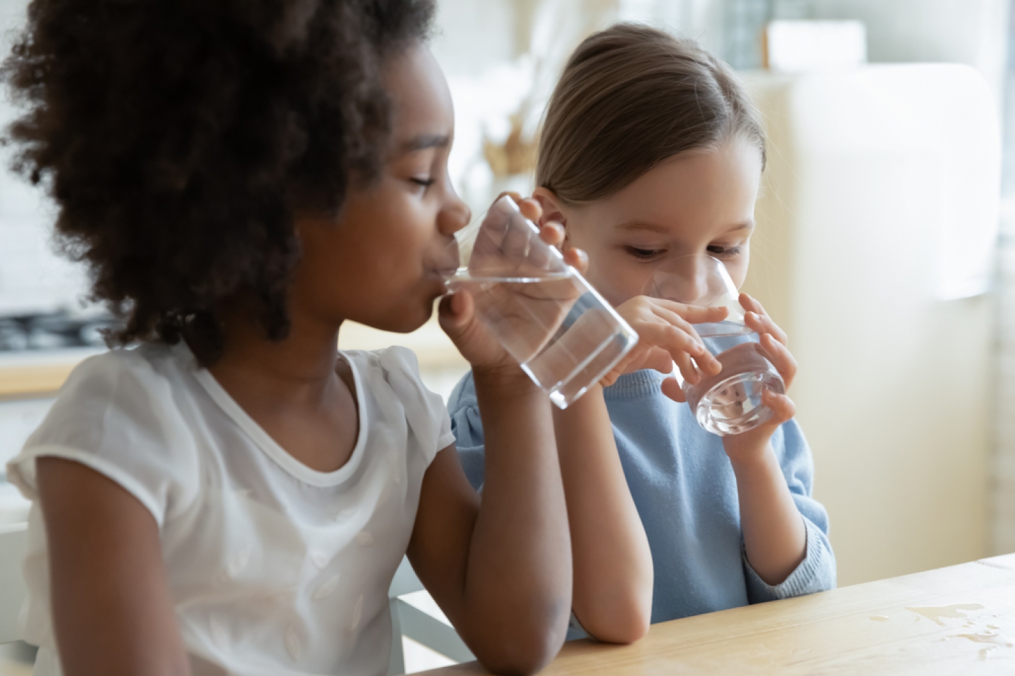 Two little girls sit at table in kitchen feels thirsty drink clean still natural or mineral water close up image.