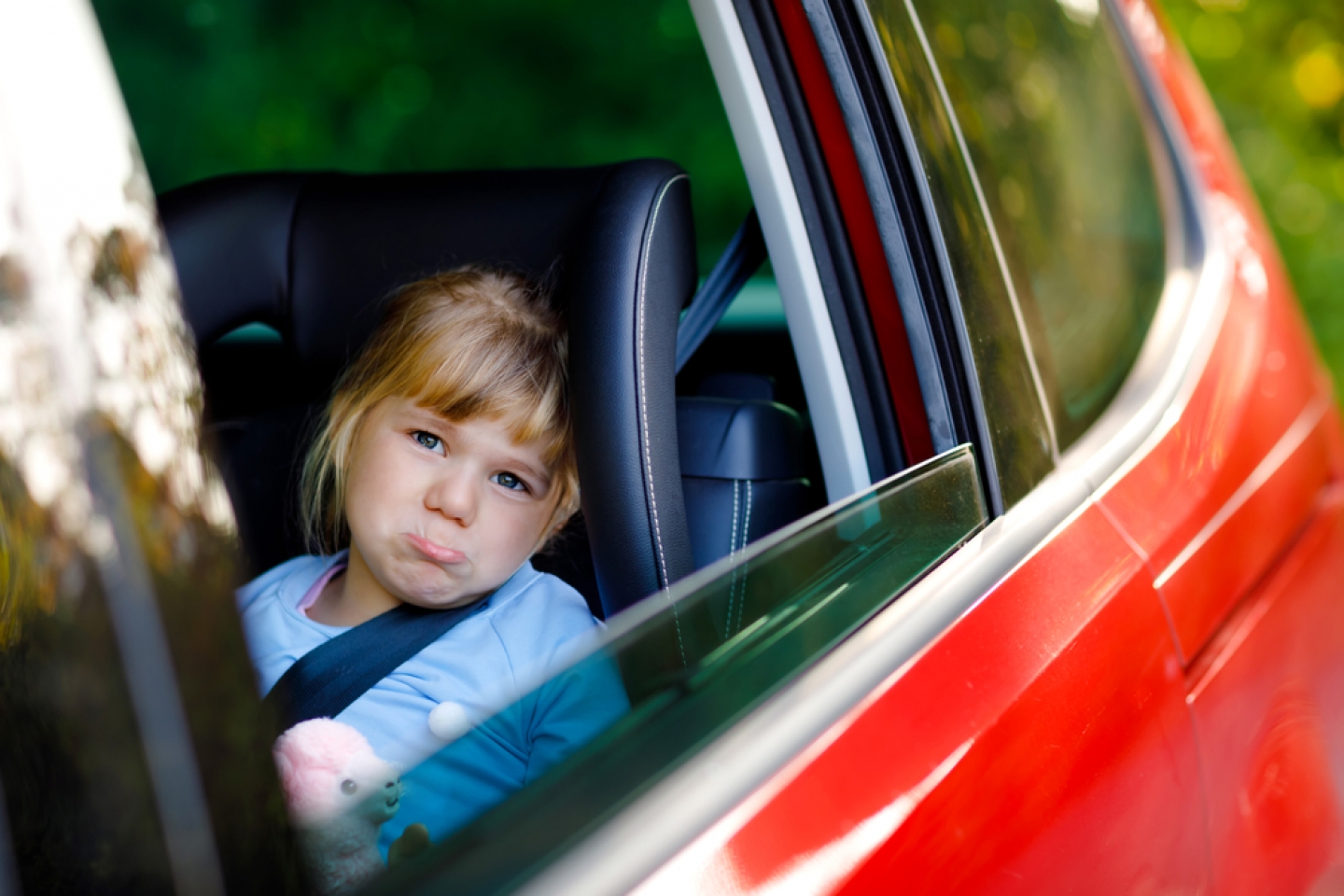 Sad upset little kid girl sitting in car in traffic jam during going for summer vacation with his parents.
