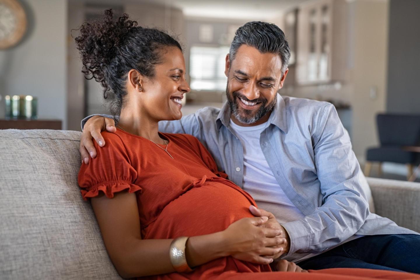 Mid adult couple expecting a baby while husband caresses the belly of his pregnant african woman. Lovely indian man touching belly of his girlfriend and feeling baby movement.