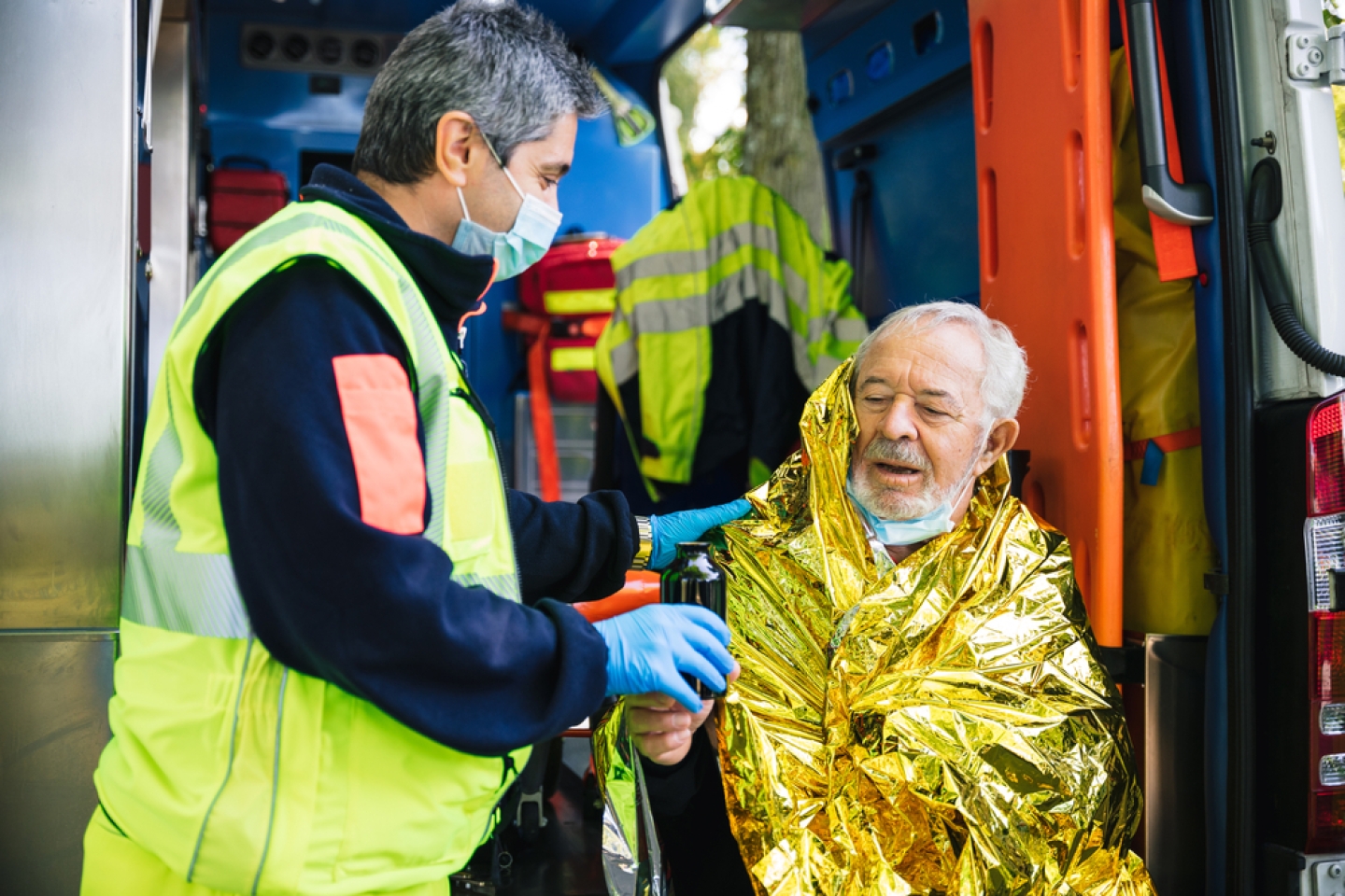 Paramedic rescues an elderly person in distress with an ambulance by covering him with a thermal blanket and making him drink a hot drink 