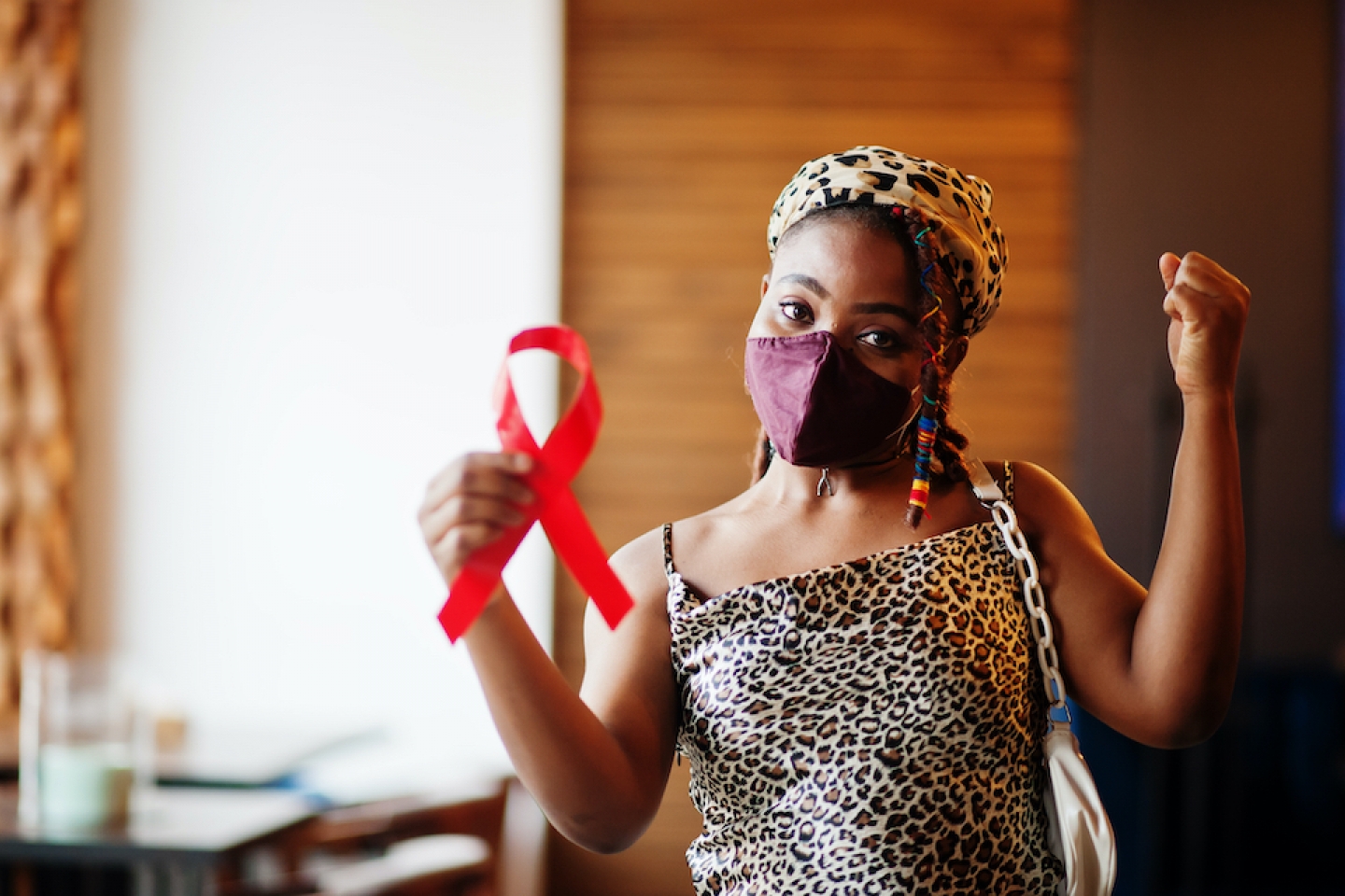 black woman with mask on holding up red ribbon for HIV awareness