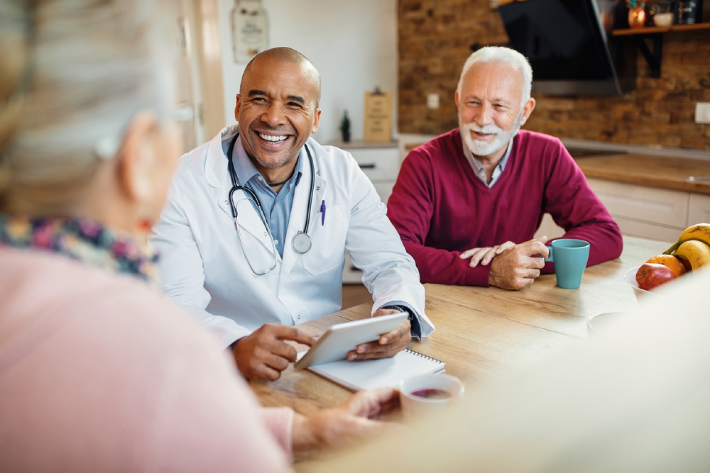 Happy black doctor using touchpad and communicating with a senior couple while visiting them at home