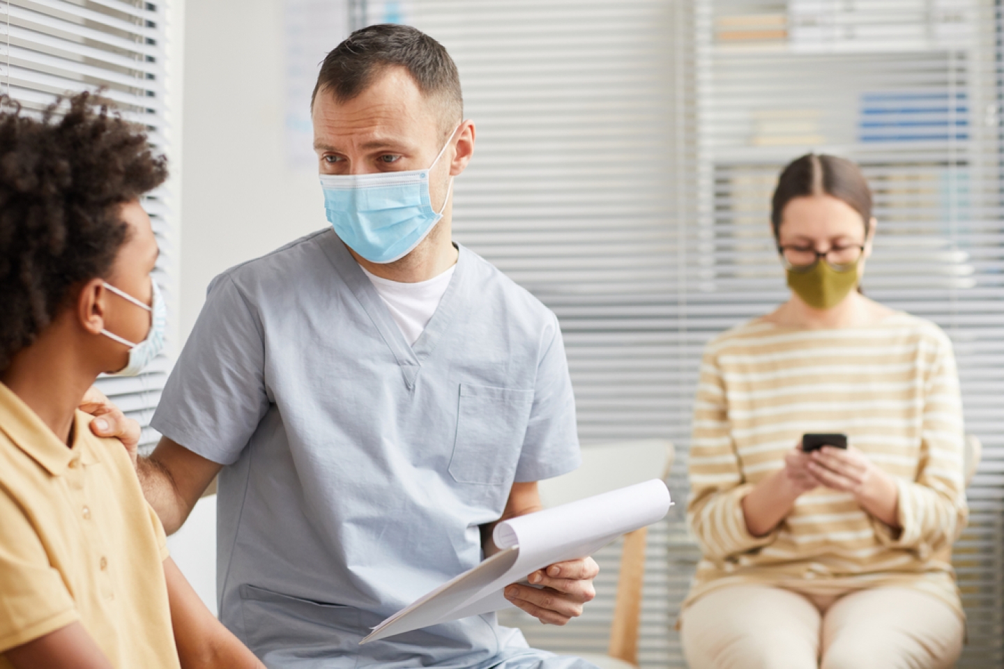 Portrait of caring male doctor talking to boy waiting in line at medical clinic.