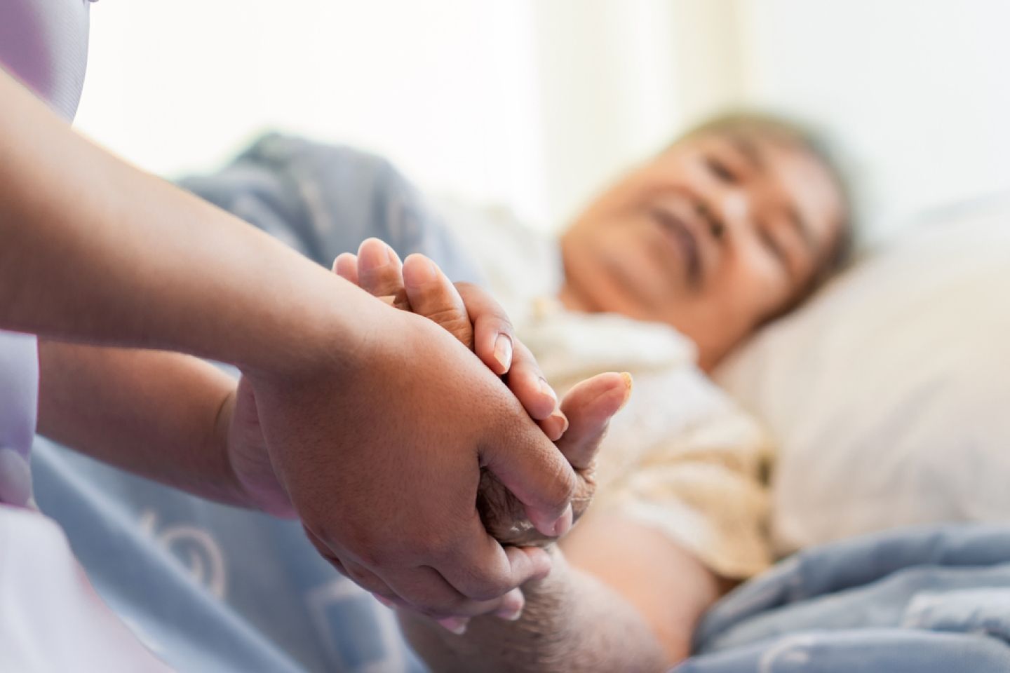 asian female home nursing holding hand of older lady on the bed and encouraging patient