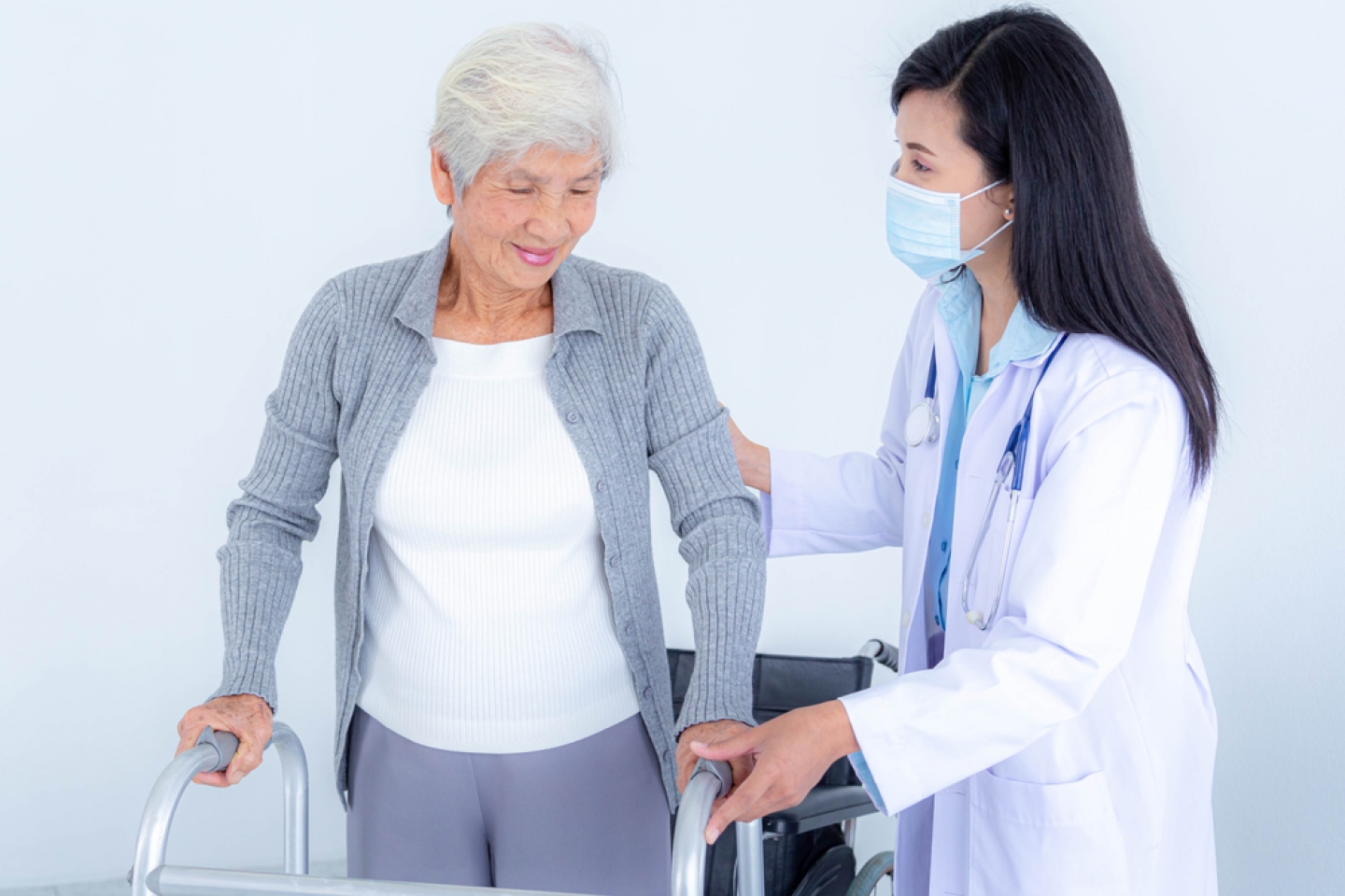 Female doctor wearing medical mask supporting senior woman by using walker.