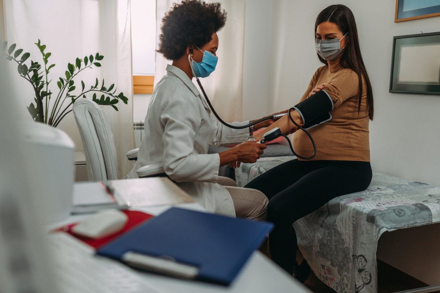 A pregnant woman during a routine check up with her doctor. Doctor is measuring pressure to her while they are wearing face masks