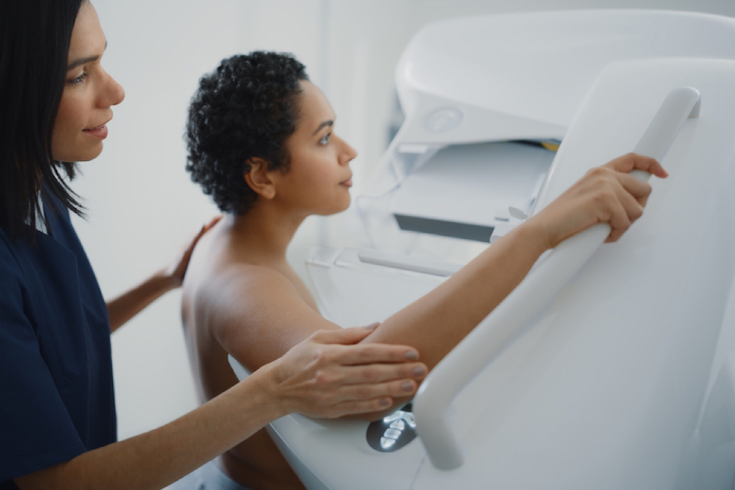  Friendly Female Doctor Explains the Mammogram Procedure to a Topless Latin Female Patient with Curly Hair Undergoing Mammography Scan.
