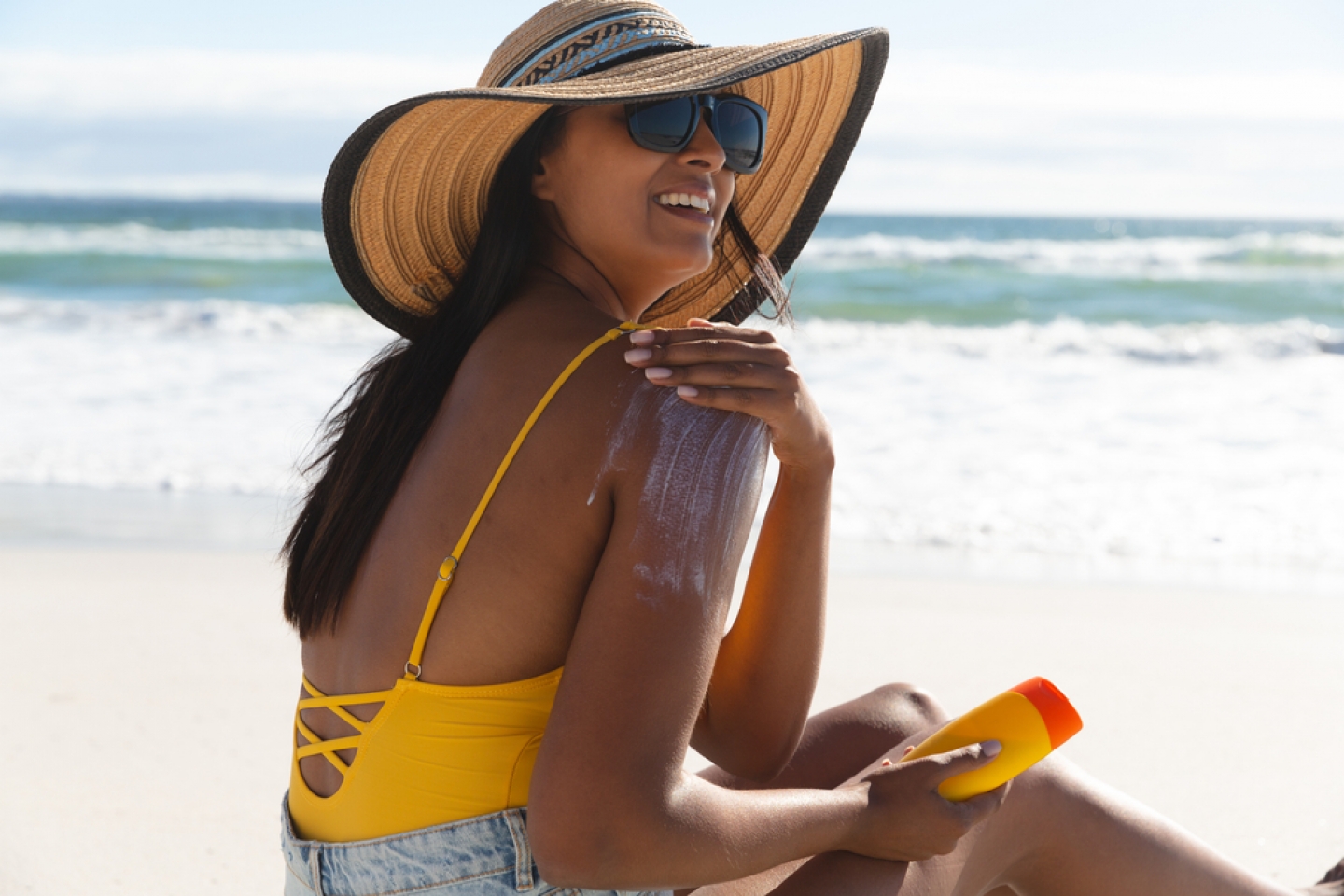 Smiling mixed race woman on beach holiday using sunscreen cream. healthy outdoor leisure time by the sea.