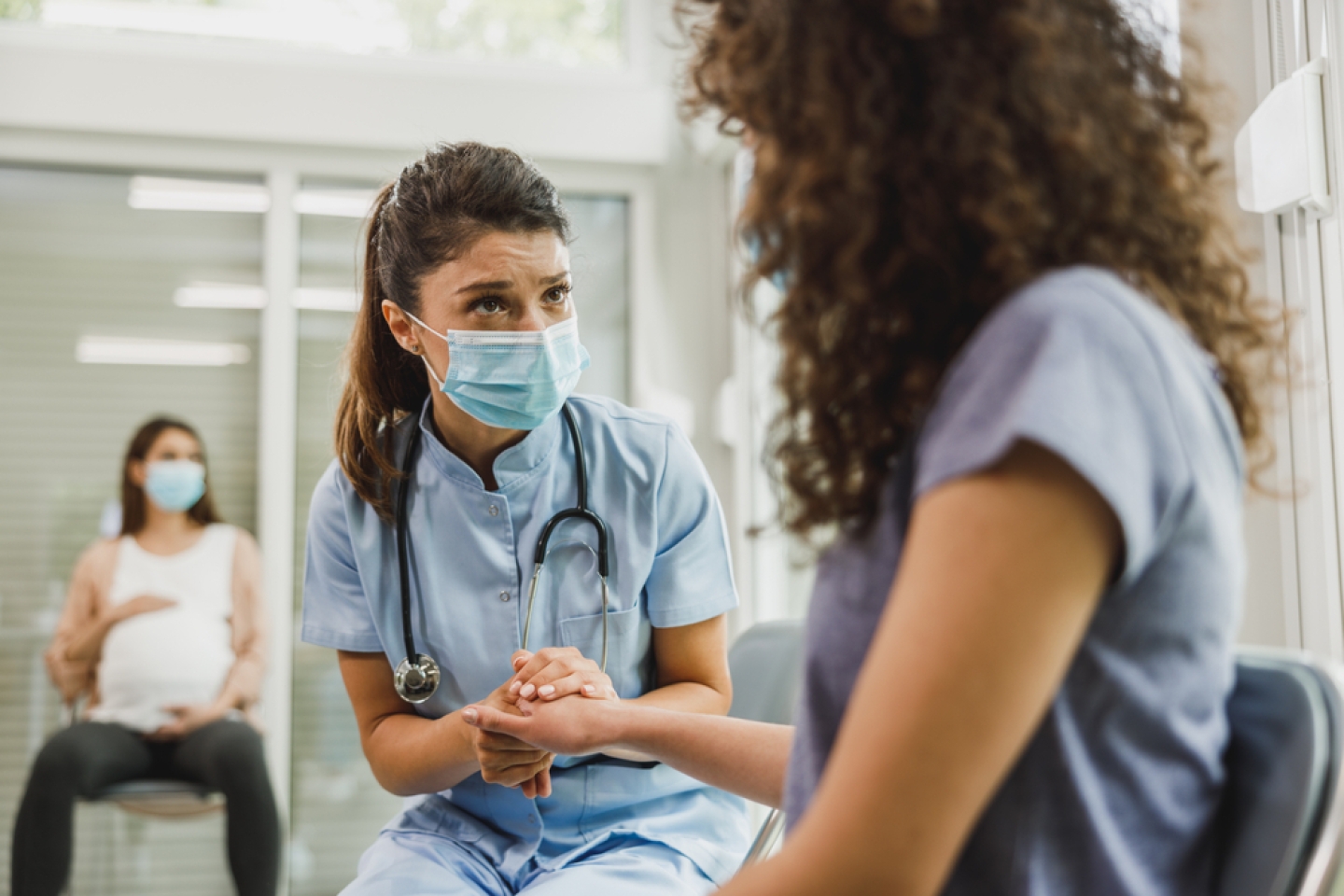 Nurse talking to African American teenager girl in a waiting room while she waits for gynecologist check up.