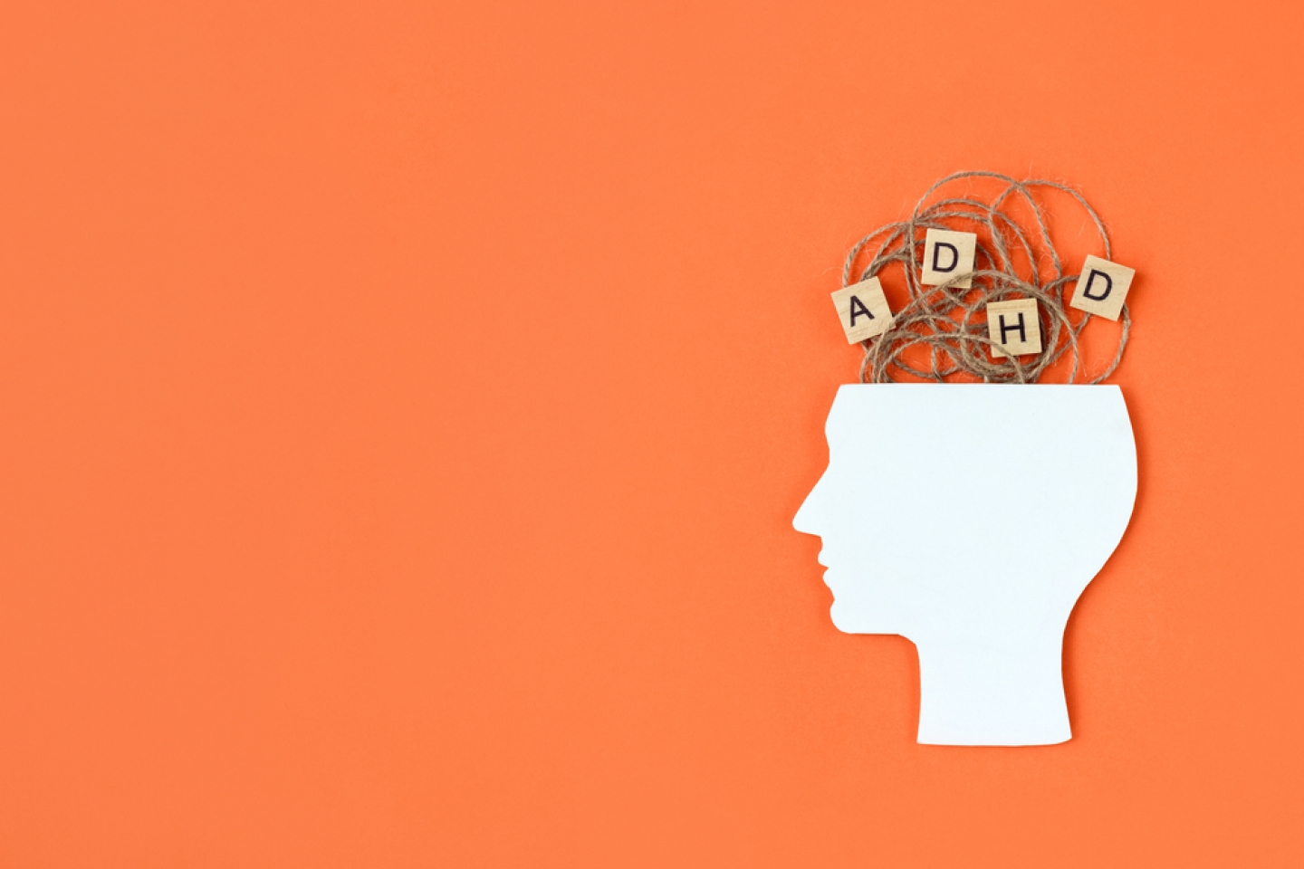 Silhouette of human head and wooden blocks with the letters ADHD on orange background.