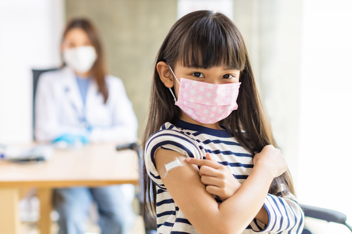 Young asian doctor wearing gloves and isolation mask is making a COVID-19 vaccination in the shoulder of child patient at hospital.