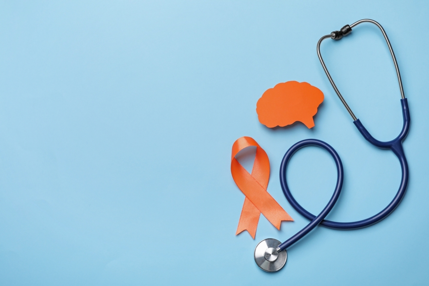 Orange ribbon, stethoscope and paper brain cutout on light blue background
