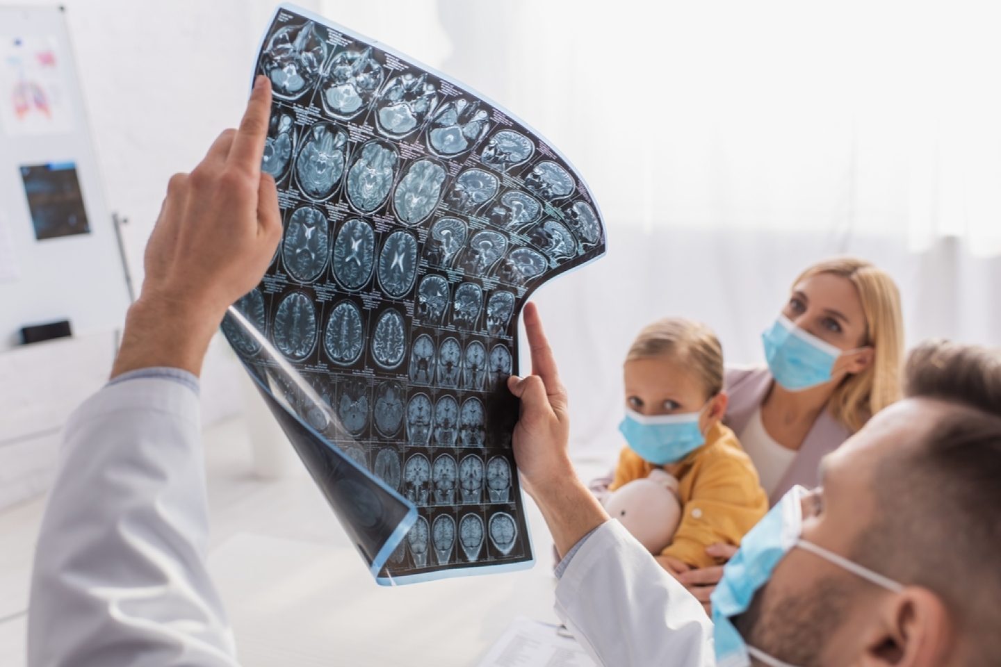 Blurred pediatrician holding mri scan near mother and kid in medical masks