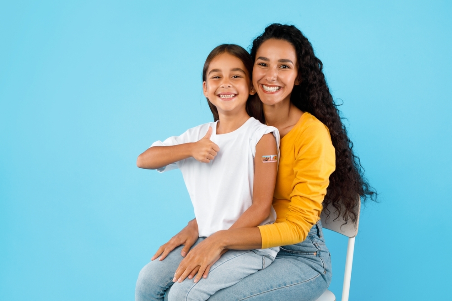 Arabic Girl And Her Mom Showing Vaccinated Arm And Thumbs Up Gesture After Covid-19 Vaccination Sitting Over Blue Background, Studio Shot.