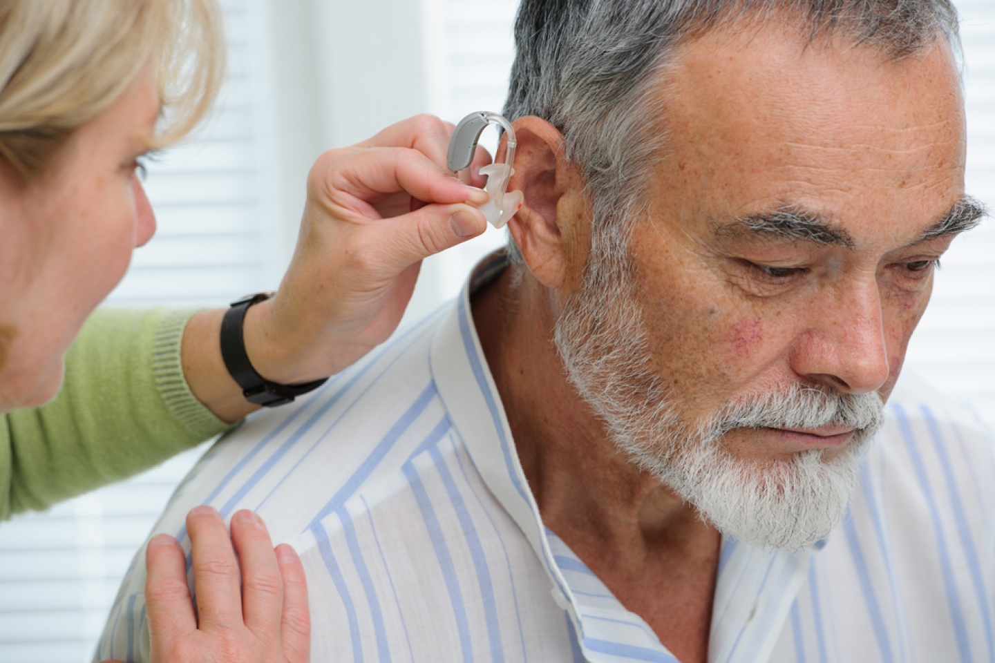 Photo of doctor inserting hearing aid in senior's ear