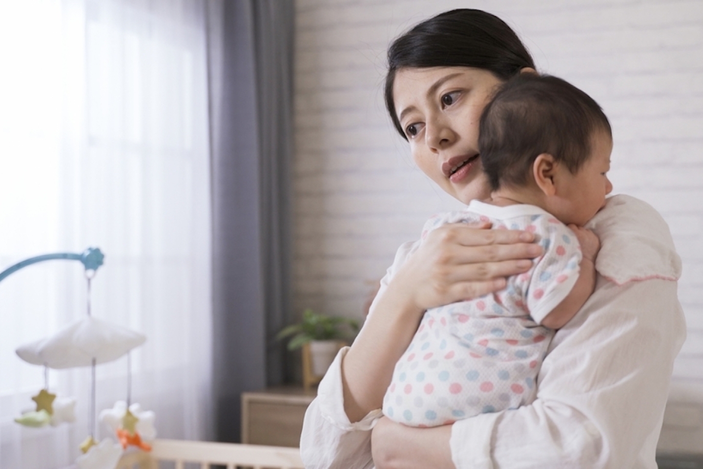 New mother is standing up from the bed and holding her baby properly while burping in the bedchamber at home.