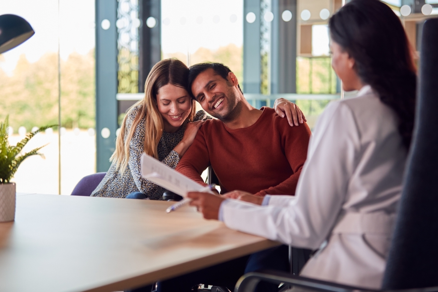 Woman Doctor Discussing Test Results With Smiling Couple n Hospital