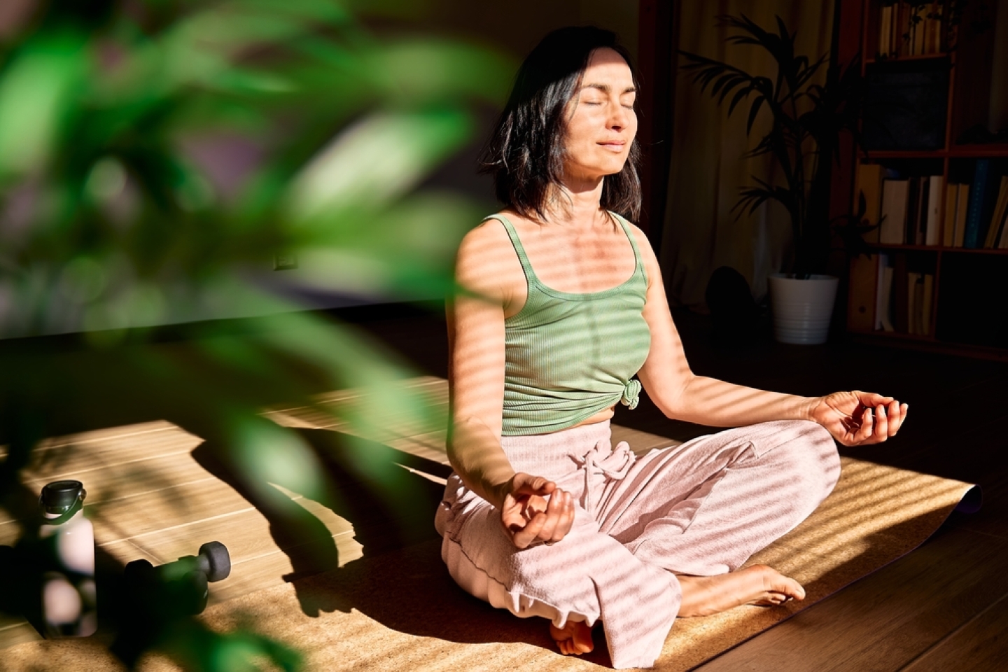 Woman practicing yoga and meditation at home sitting in lotus pose on yoga mat, relaxed with closed eyes. Mindful meditation concept. Wellbeing.