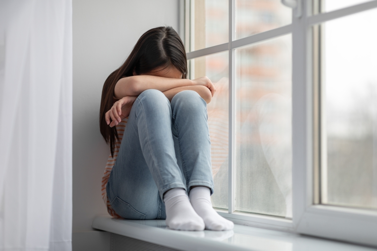 Upset asian school-aged girl sitting on windowsill and crying, female kid feeling lonely or insulted, got quarrel with parents or friends, home interior, panorama with copy space