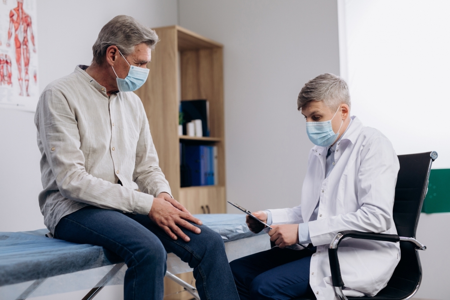 Elderly patient wearing medical mask talking to male family therapist during regular doctors appointment.