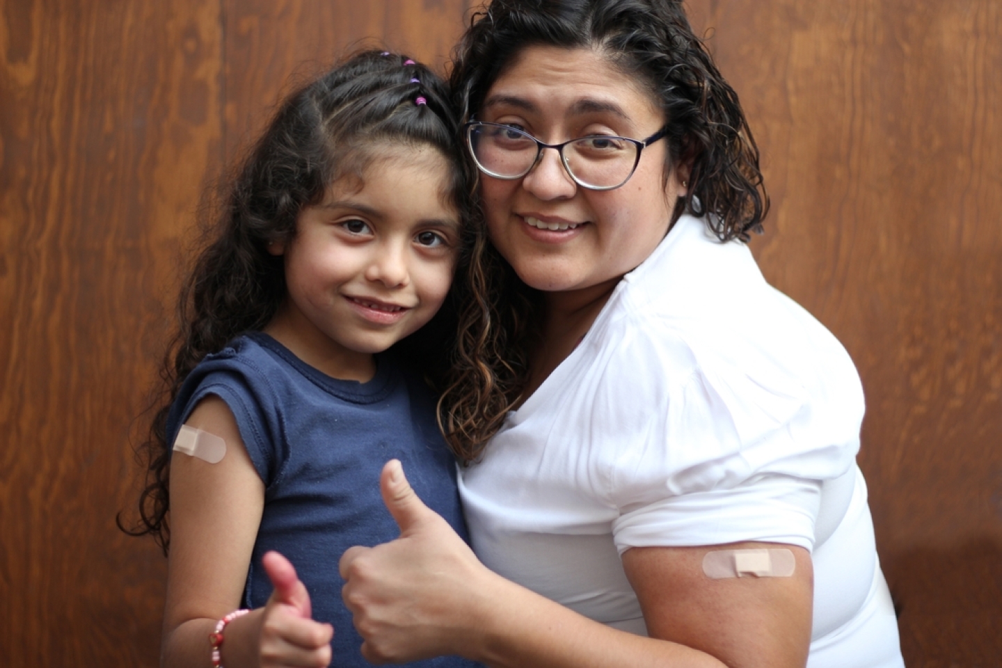 Happy and hugging Latin mom and daughter show their recently vaccinated arms against Covid-19 in the new normality due to the Coronavirus pandemic