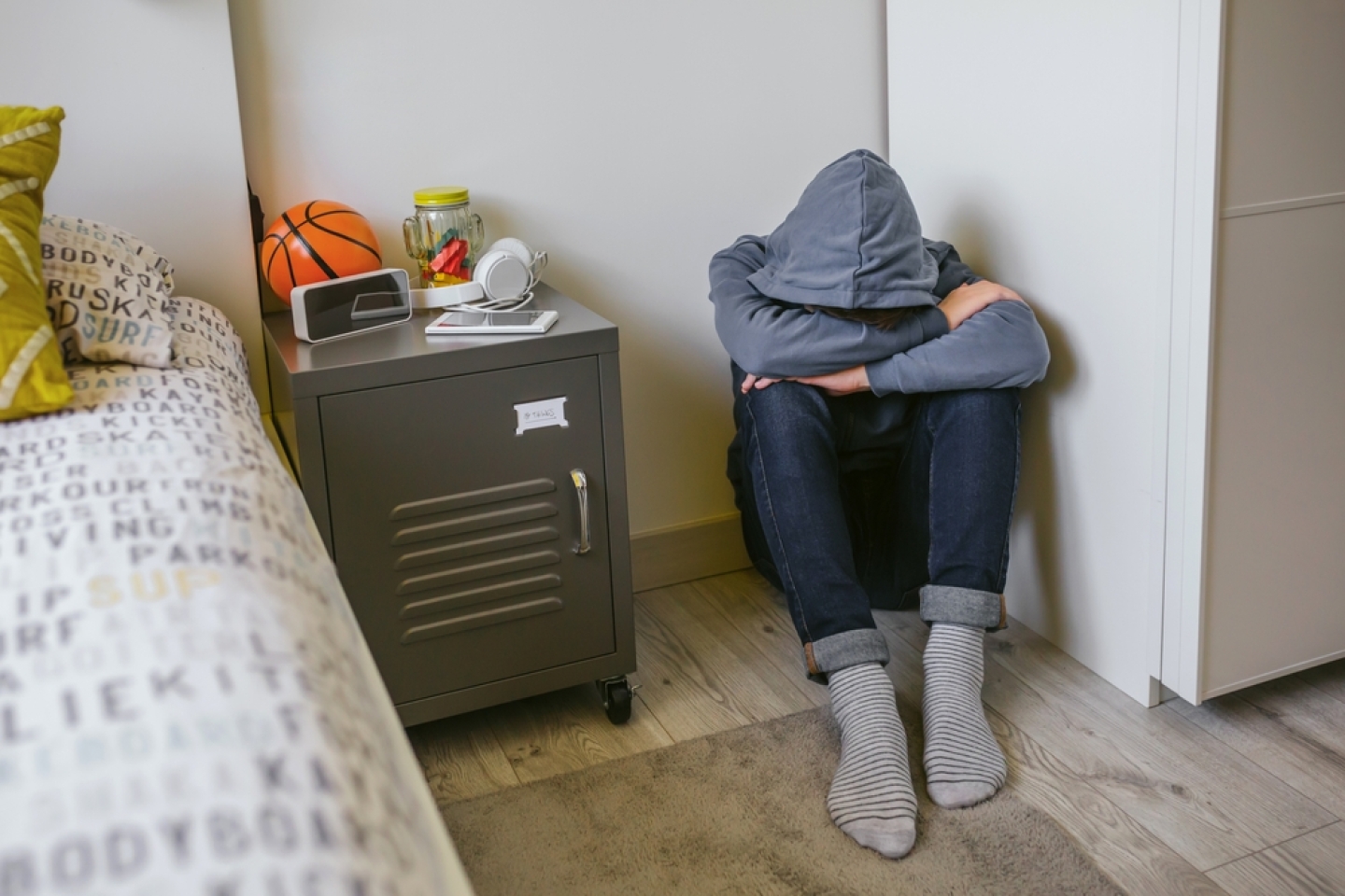 Unrecognizable teenager boy with anxiety sitting on the floor of his bedroom with his head resting on his arms