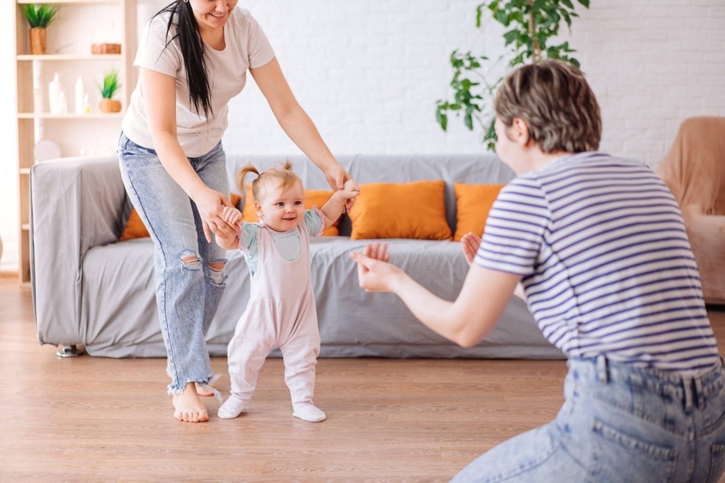a little girl takes her first steps with the help of her parents.