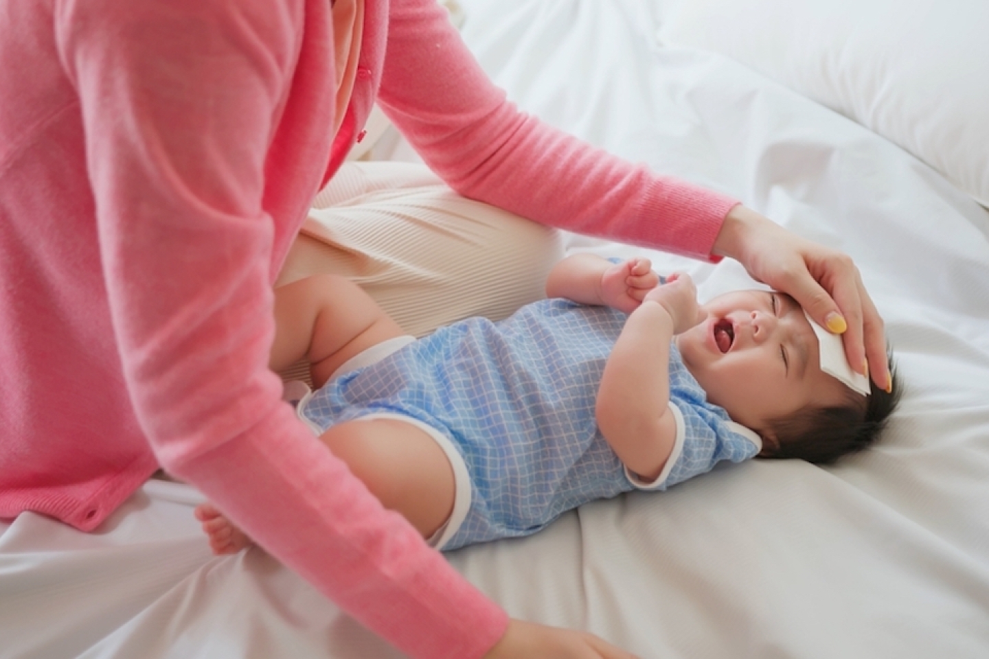 authentic shot of asian baby has fever and his mother checks body temperature by thermometer on bed
