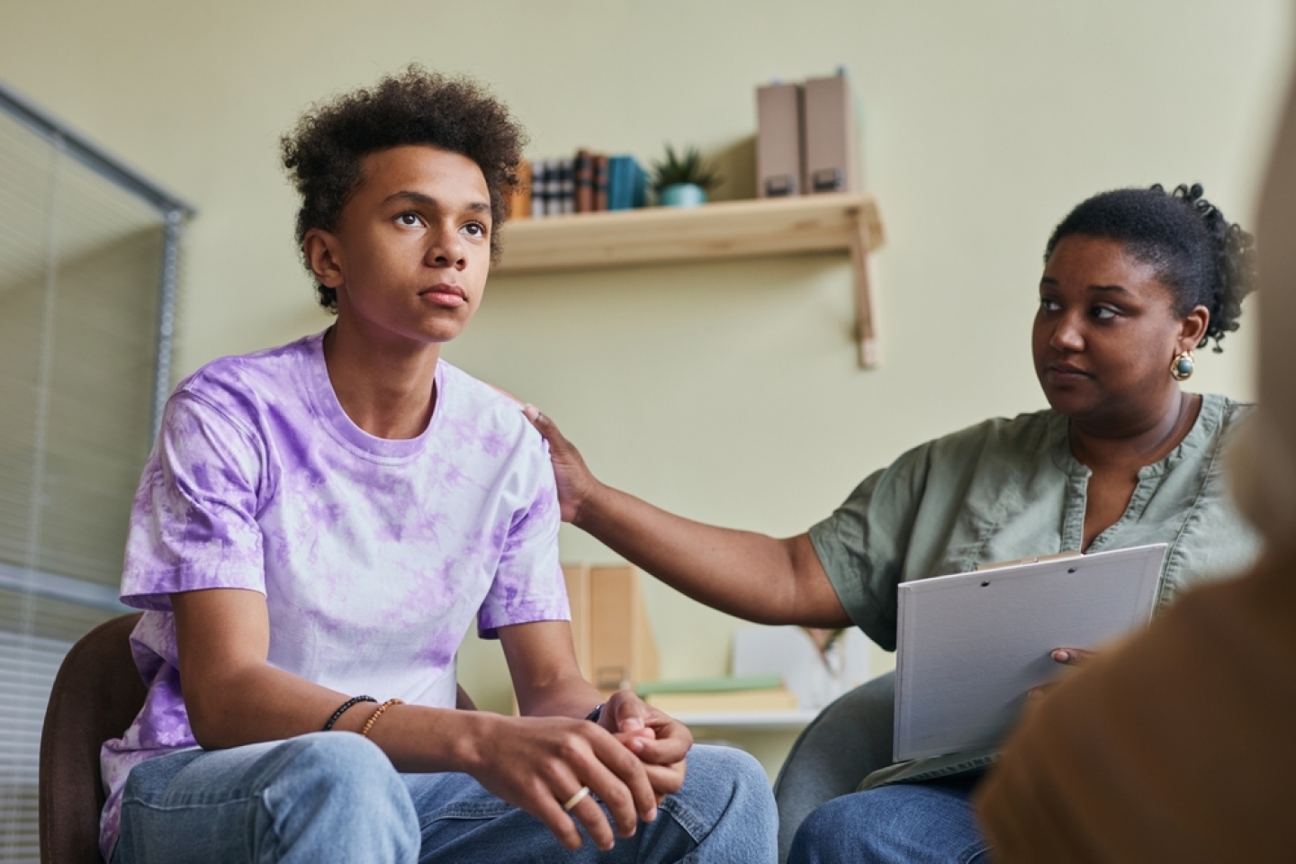 African teenage boy talking during group therapy session with psychologist supporting him