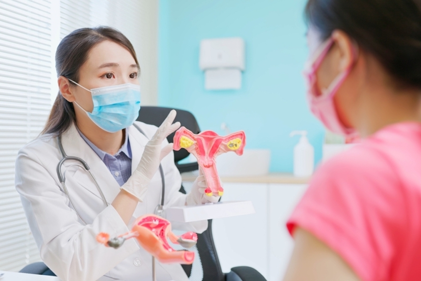 asian female doctor wear white coat and face mask explaining uterus model to woman in hospital