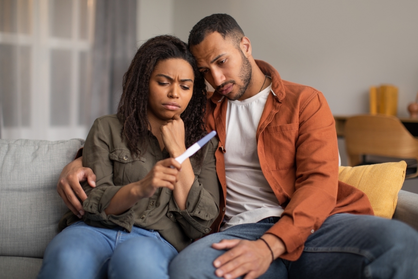 Black Couple Holding Negative Pregnancy Test Hugging Sitting On Couch At Home.