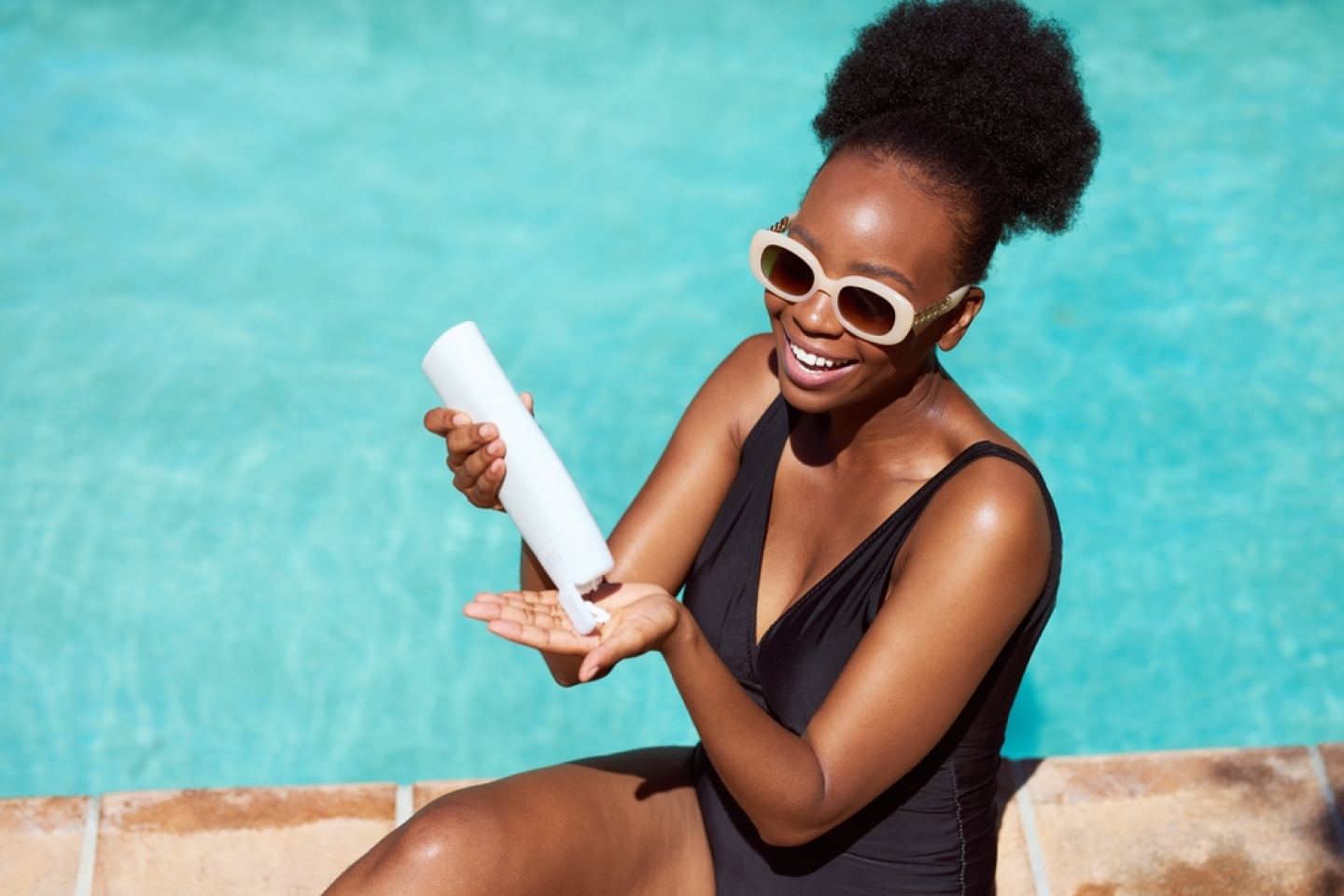 woman applies sunscreen sitting by pool in summer sun