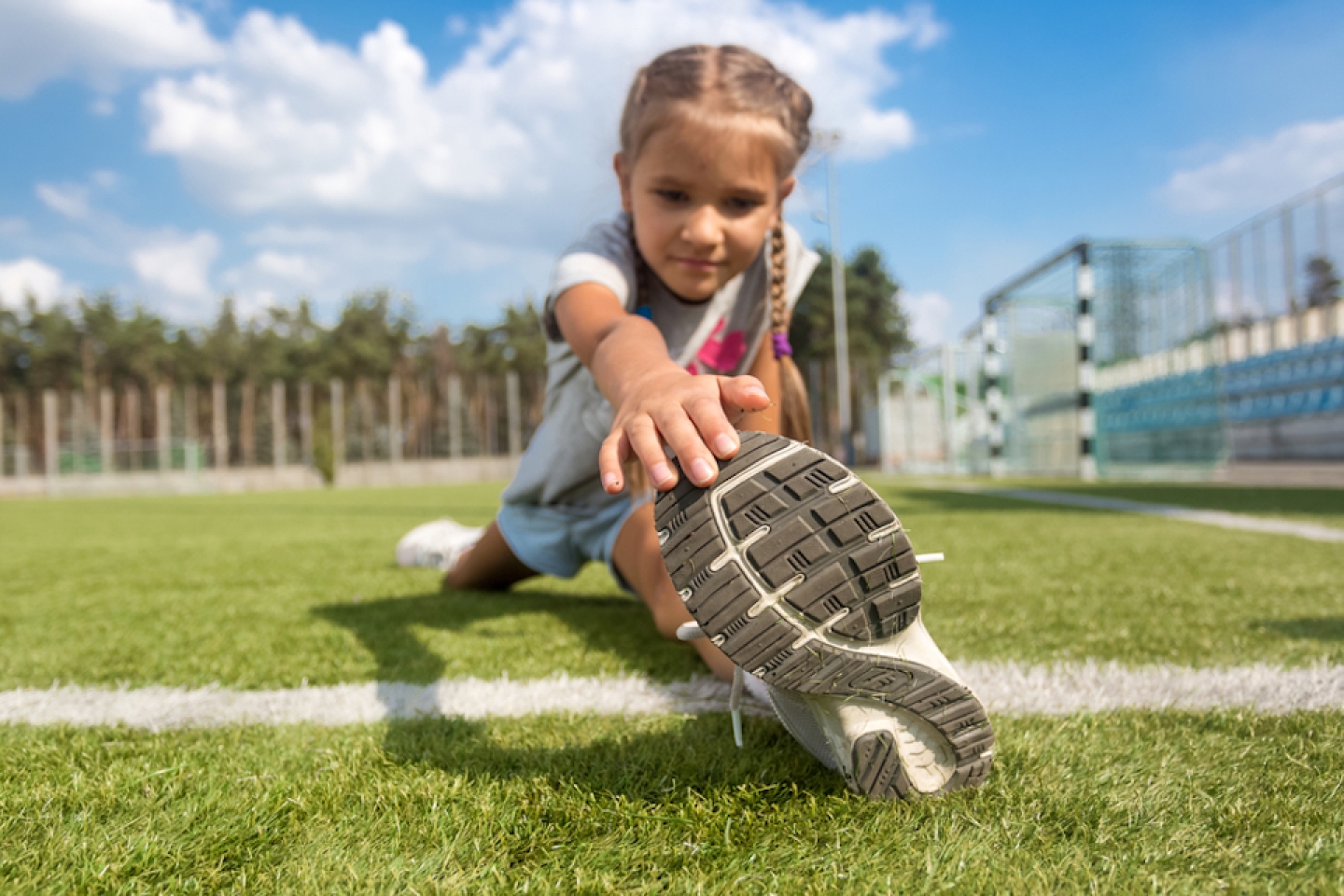 Closeup shot of young girl stretching legs on soccer field at sunny day