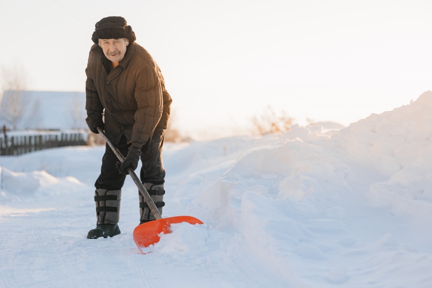 Elderly man cleaning snow with shovel after snowstorm, sunlight.