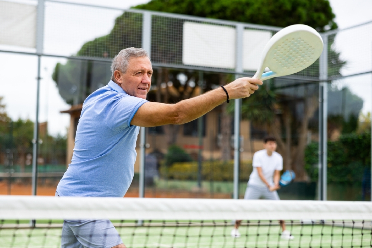 Focused aged man playing friendly paddleball match on outdoor summer court. Senior people sports concept..