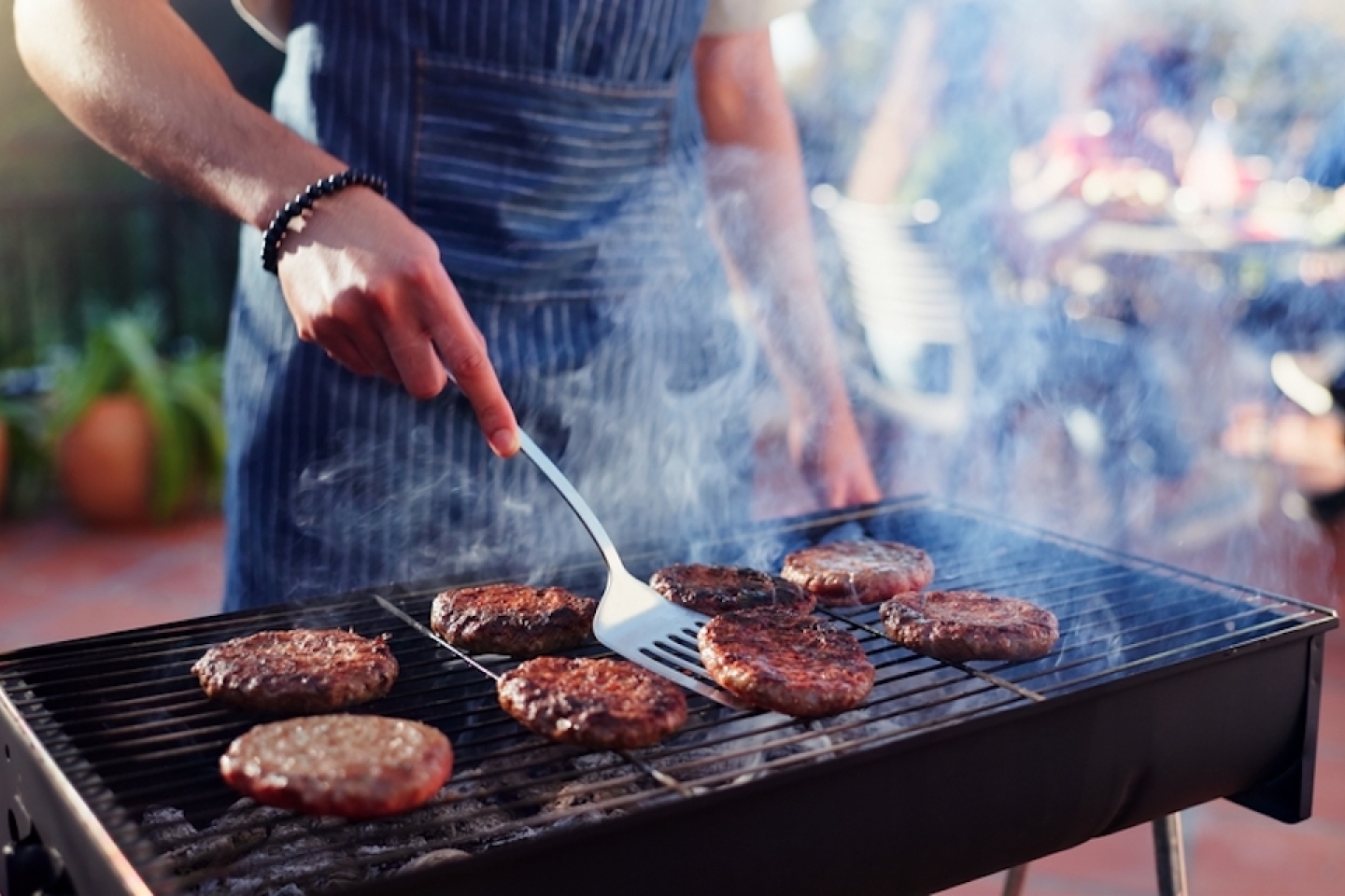 Barbecue, cooking and man with burgers outdoor backyard for meal at reunion, social event or lunch on terrace.