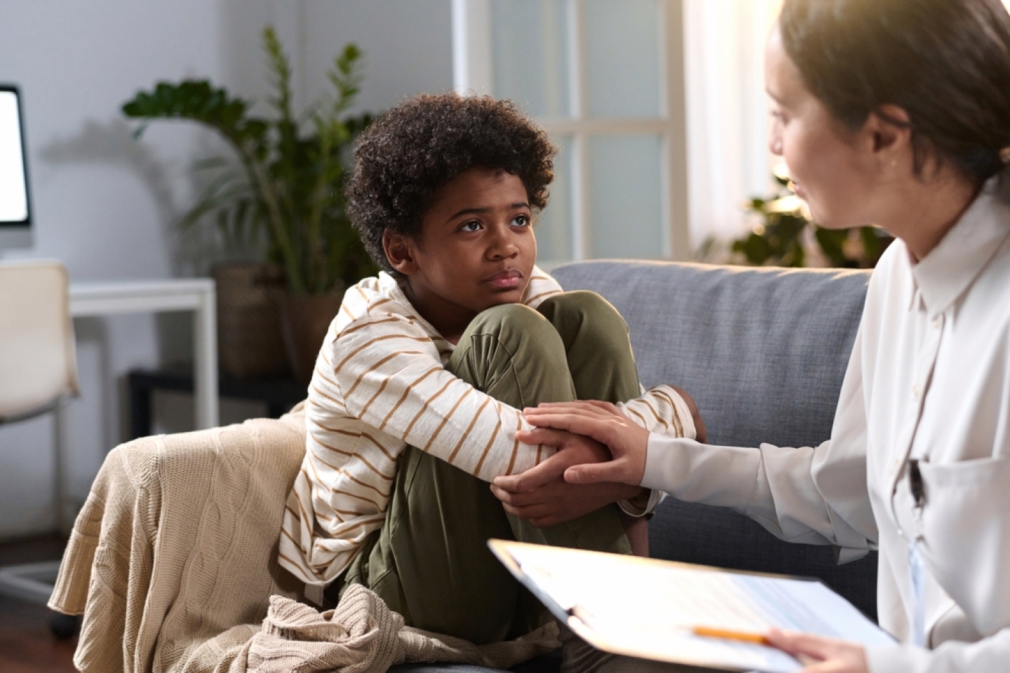 Portrait of young African American boy listening to caring psychologist in therapy session for children