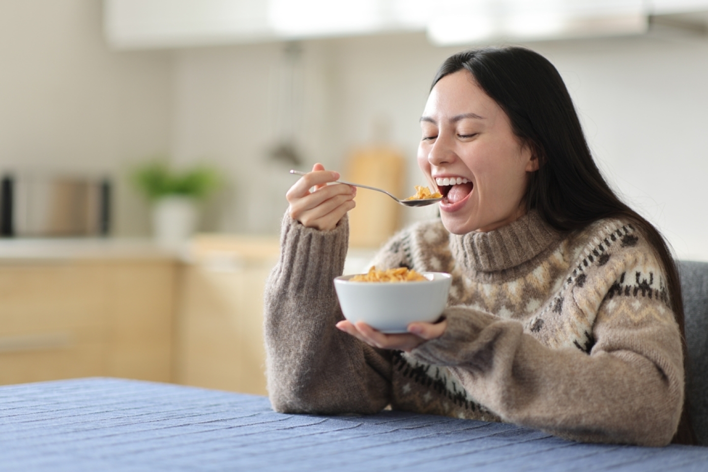 Happy asian woman eating cereals in winter in the kitchen at home