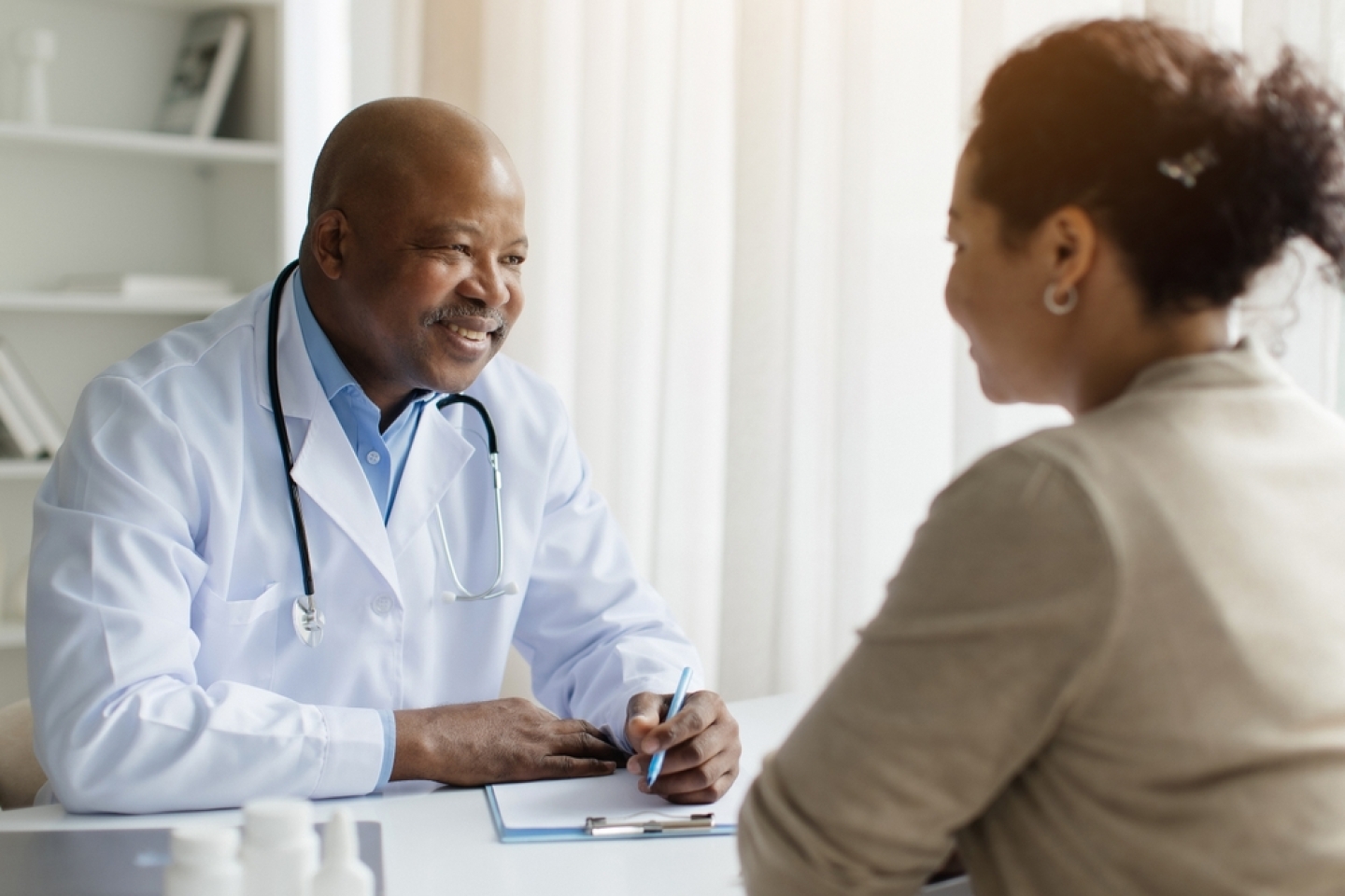 Smiling Black Doctor In Uniform Consulting Female Patient During Meeting In Clinic